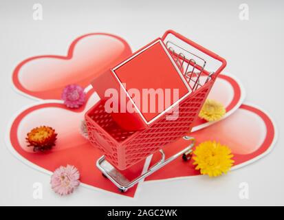 Shopping Cart mit roter Geschenkbox auf einem Hintergrund von Papier Herzen Stockfoto