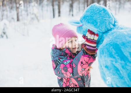 Nahaufnahme eines glücklichen kleinen Mädchens, das die Wangen kneifen soll Von einer Frau in einem flauschigen blauen Kostüm Stockfoto