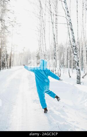 Vertikale Aufnahme einer Person in einem blauen flauschigen Kostüm Glücklich im verschneiten Wald spazieren Stockfoto