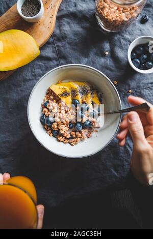 Mädchen hält eine Schüssel mit Frühstück crunchy Müsli, frischen Heidelbeeren, Mango und Chia Samen. Flach, Ansicht von oben, das gesunde Essen. Stockfoto