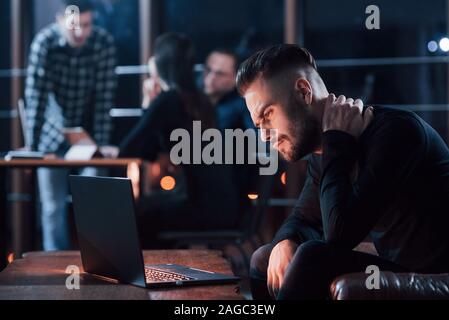 Probleme mit dem Hals. Team der jungen Unternehmer arbeitet an ihrem Projekt in der Nacht im Büro Stockfoto