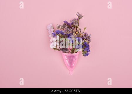 Blick von oben auf die rosa Kunststoff Menstruationsschale mit Wildblumen isoliert auf Rosa Stockfoto