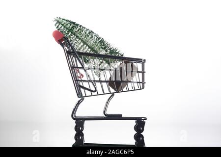 Seitenansicht des Mini Weihnachtsbaum in kleinen Einkaufswagen auf hellen Hintergrund Stockfoto