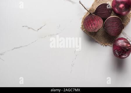 Blick von oben auf die roten Zwiebeln und Rote Beete Hälften auf Marmor Oberfläche mit hessischen Stockfoto