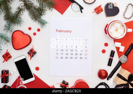 Februar Kalender Seite, Kaffee mit Marshmallow, Smartphone, Tanne, Armbanduhr, Armreifen, Christbaumkugeln, rotes Papier, Armbanduhr auf w isoliert Stockfoto