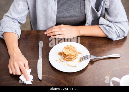 Ansicht von oben von Frau sitzt in der Nähe von Tabelle mit süßen Pfannkuchen auf Platte Stockfoto