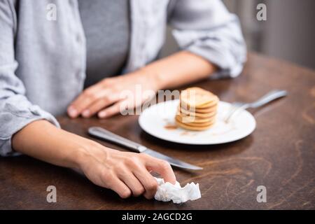 7/8-Ansicht von Frau mit Serviette in der Nähe von leckeren Pfannkuchen zu Hause Stockfoto