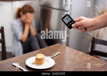 7/8-Ansicht von Mann, Blutzuckermessgeräte, die mit den Nummern in der Nähe von Frau Stockfoto