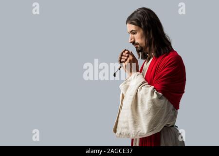 Religiöse Mann hält Rosenkranz betend auf Grau isoliert Stockfoto