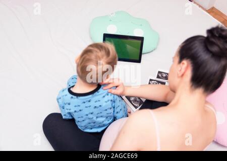 Neugierig schön darkeyed junge Gefühl sehr interessiert, während playingwoth seine schwangere Mutter. Bitte warten, bis die kleine Schwester. Stockfoto