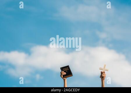 7/8-Ansicht von Mann mit Bibel und Kreuz gegen den blauen Himmel mit Wolken Stockfoto