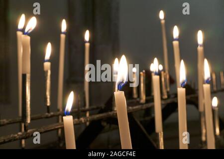 Viele brennende weiße Kerzen in der Kirche vor einem dunklen Hintergrund. Stockfoto