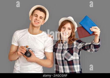 Reise und Tourismus. Junger Mann mit Kamera und Frau mit Pässen in Hüte isoliert auf Grau lächelnd freudige stehend Stockfoto