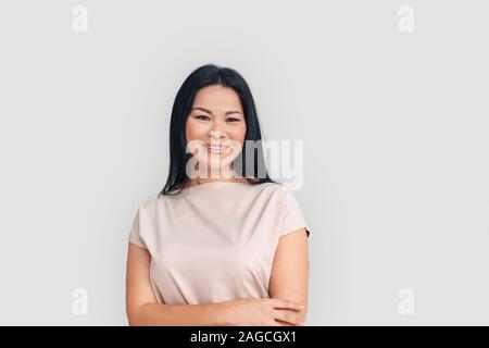 Freestyle. Asiatische Frau, die isoliert auf weißem verschränkte Arme lächelte zuversichtlich Stockfoto