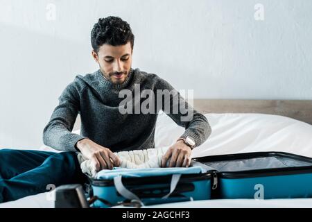 Stattliche rassische Bi - Mann in Pullover packen Reisetasche in der Wohnung Stockfoto