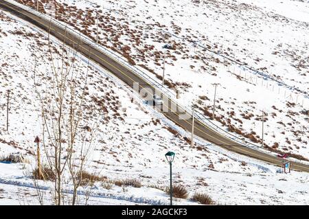 Hochwinkelaufnahme eines Autos, das auf einer von schneebedeckten Feldern umgebenen Straße in Andes Cordillera, Chile fährt Stockfoto