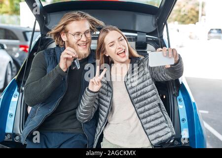 Reisen. Junges Paar mit dem Auto sitzen im Kofferraum unter selfie Foto Reisen auf dem Smartphone lächelt Fröhlich Stockfoto