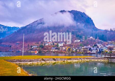 TRAUNKIRCHEN, Österreich - 22. Februar 2019: Der Zug fährt entlang der bewölkt Berghang, mit Häuser der kleinen Stadt am Ufer des Trauns abgedeckt Stockfoto