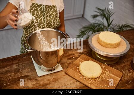 7/8-Ansicht von konditor hinzufügen Mehl in Schüssel neben Kuchen Schichten auf Tabelle Stockfoto