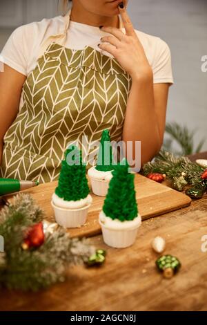 7/8-Ansicht von konditor stand neben Weihnachtsbaum Cupcakes und Dekorationen auf Tisch Stockfoto