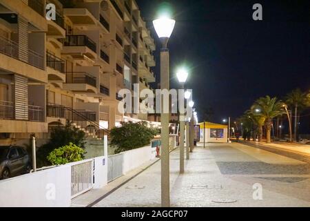 Quarteira, Portugal Promenade bei Nacht, mit Wohnungen auf der linken Seite und Palmen und der Strand auf der rechten Seite. Stockfoto