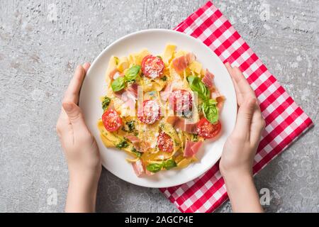 Teilweise mit Blick auf die Frau mit Platte mit Pappardelle mit Tomaten, Basilikum und Prosciutto auf plaid Serviette auf graue Oberfläche Stockfoto