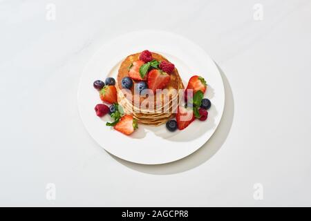 Leckere Pfannkuchen mit Honig, Blaubeeren und Erdbeeren auf Platte auf Marmor weiß Oberfläche Stockfoto