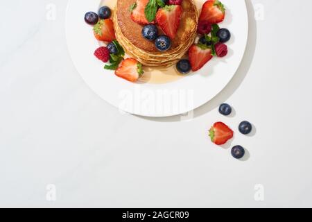 Blick von oben auf die leckere Pfannkuchen mit Honig, Blaubeeren und Erdbeeren auf Marmor weiß Oberfläche Stockfoto