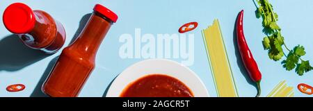 Blick von oben auf die würzigen Tomatensauce neben rohe Spaghetti und Chili auf blauem Hintergrund, Panorama-Aufnahme ein. Stockfoto