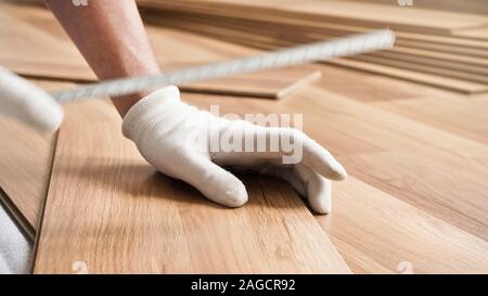 Installation von Laminat, Detail auf den Menschen Hände in weißen Handschuhen, holding Maßband über Holz Fliesen Stockfoto