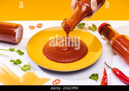 7/8-Ansicht von Frau gießen Chili Sauce auf Platte mit Chili Peppers und Spaghetti auf weisse Oberfläche isoliert auf Gelb Stockfoto