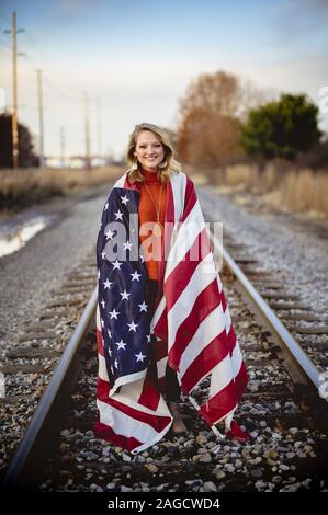 Vertikale Aufnahme einer Frau, die auf Bahngleisen mit steht Die usa flaggen um sie herum Stockfoto