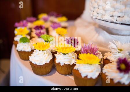 Viele Cupcakes mit verschiedenen Blumen auf einem Weißer Tisch mit verschwommenem Hintergrund Stockfoto