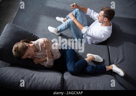 Ansicht von oben der weinenden Frau liegt auf einem Sofa und Mann sitzt auf dem Boden Stockfoto