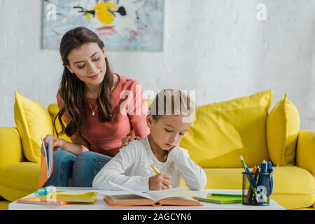 Selektiver Fokus der gerne Babysitter sitzt auf einem Sofa und bei cute kid Studium zu Hause suchen Stockfoto