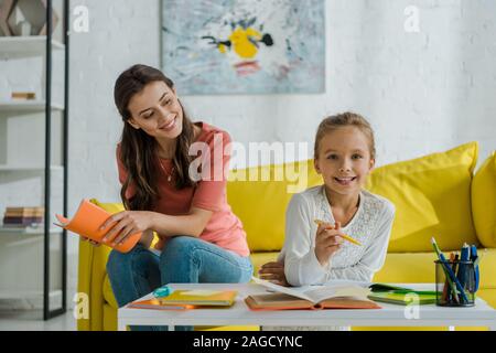 Selektiver Fokus der gerne Babysitter holding Notebook beim Sitzen auf dem Sofa und cute kid Studium zu Hause suchen Stockfoto