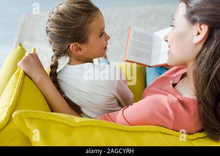 Selektiver Fokus Kind sitzt auf einem Sofa mit glücklichen Babysitter holding Buch Stockfoto