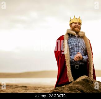 Portrait von Mittel-erwachsener Mann mit Mantel und Krone während am Strand. Stockfoto