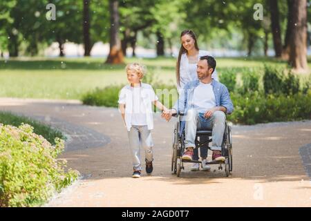 Mutter rolling Rollstuhl mit behinderten Vater im Park in der Nähe von Son Stockfoto