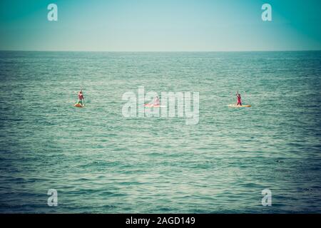 Eine Ansicht der Rückseite zwei Bikini bekleideten Frauen und ein Mann kniet, wie sie ihren Handlungsspielraum Stand up Paddle Boards auf den Pazifischen Ozean von Santa Barbara Stockfoto