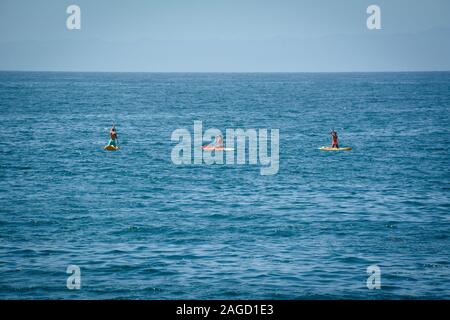 Eine Ansicht der Rückseite zwei Bikini bekleideten Frauen und ein Mann kniet, wie sie ihren Handlungsspielraum Stand up Paddle Boards auf den Pazifischen Ozean von Santa Barbara Stockfoto