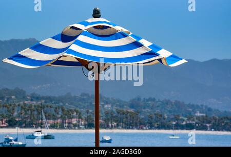 Eine Nahaufnahme von einem blau-weiß gestreiften Strand oder Sonnenschirm mit weit entfernten Segelboote im Hafen von Santa Barbara, Santa Barbara, CA, USA Stockfoto