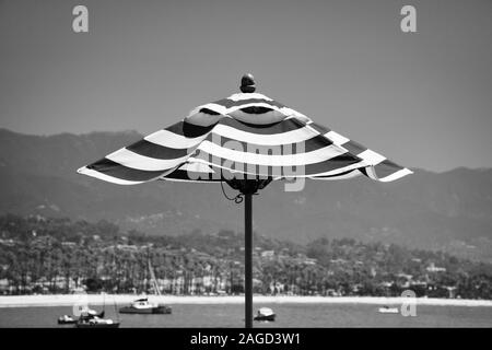 Eine Nahaufnahme von einem gestreiften Strand oder Sonnenschirm mit einem Hintergrund von Segelbooten in Santa Barbara Hafen mit in Schwarz und Weiß, Santa Barbara, CA Stockfoto