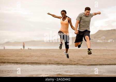 Lächelnden jungen Paar über flachem Wasser an einem Strand zu springen. Stockfoto