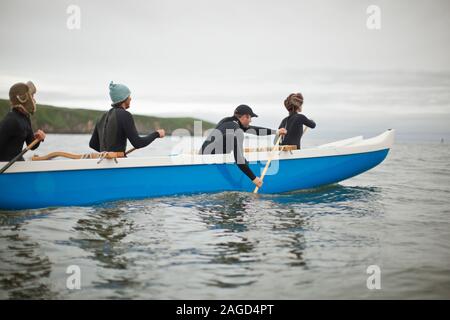 Vier junge Erwachsene zusammen Paddeln in einem Kanu auf dem See. Stockfoto