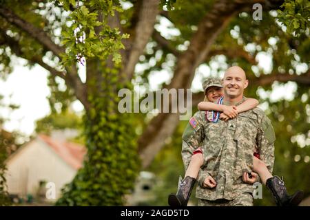 Lächelnd männlichen Soldaten piggy-backing seine junge Tochter in ihrem Hinterhof. Stockfoto