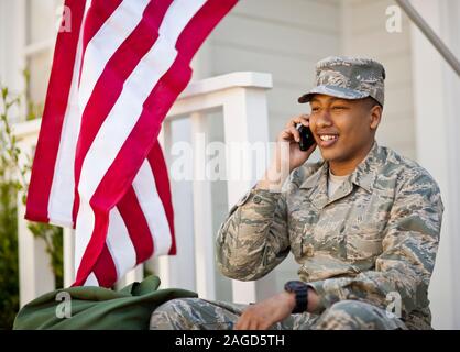 Junge erwachsene Soldaten sprechen über ein Handy auf der Veranda seines Hauses. Stockfoto