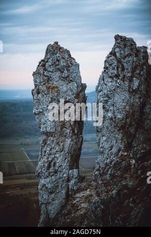 Vertikale Aufnahme von hohen Felsen mit Feldern und einer Stadt Auf dem Hintergrund unter einem blau bewölkten Himmel Stockfoto