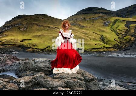 Eine junge Rotkopffrau bleibt auf einem großen Stein in der Nähe der Küste des Ozeans. Eine Lagune in der Nähe des Atlantiks. Insel Streymoy. Faröer Island. Ich habe eine Modellversion Stockfoto