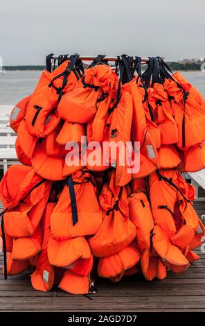 Viele orange Schwimmwesten hängen an der Zahnstange auf Pier am Meer Stockfoto